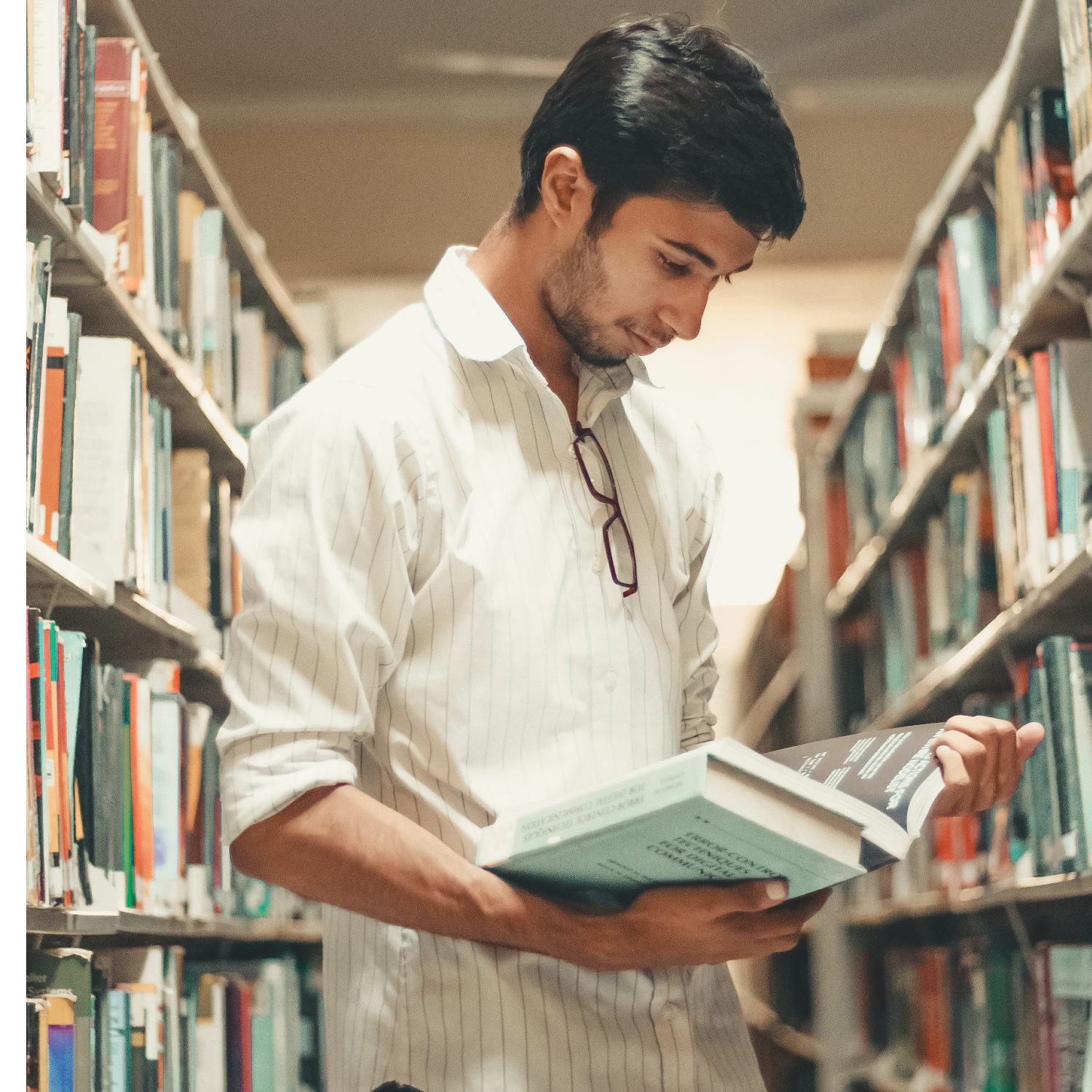 Fotografía de un joven consultando un libro en la biblioteca.