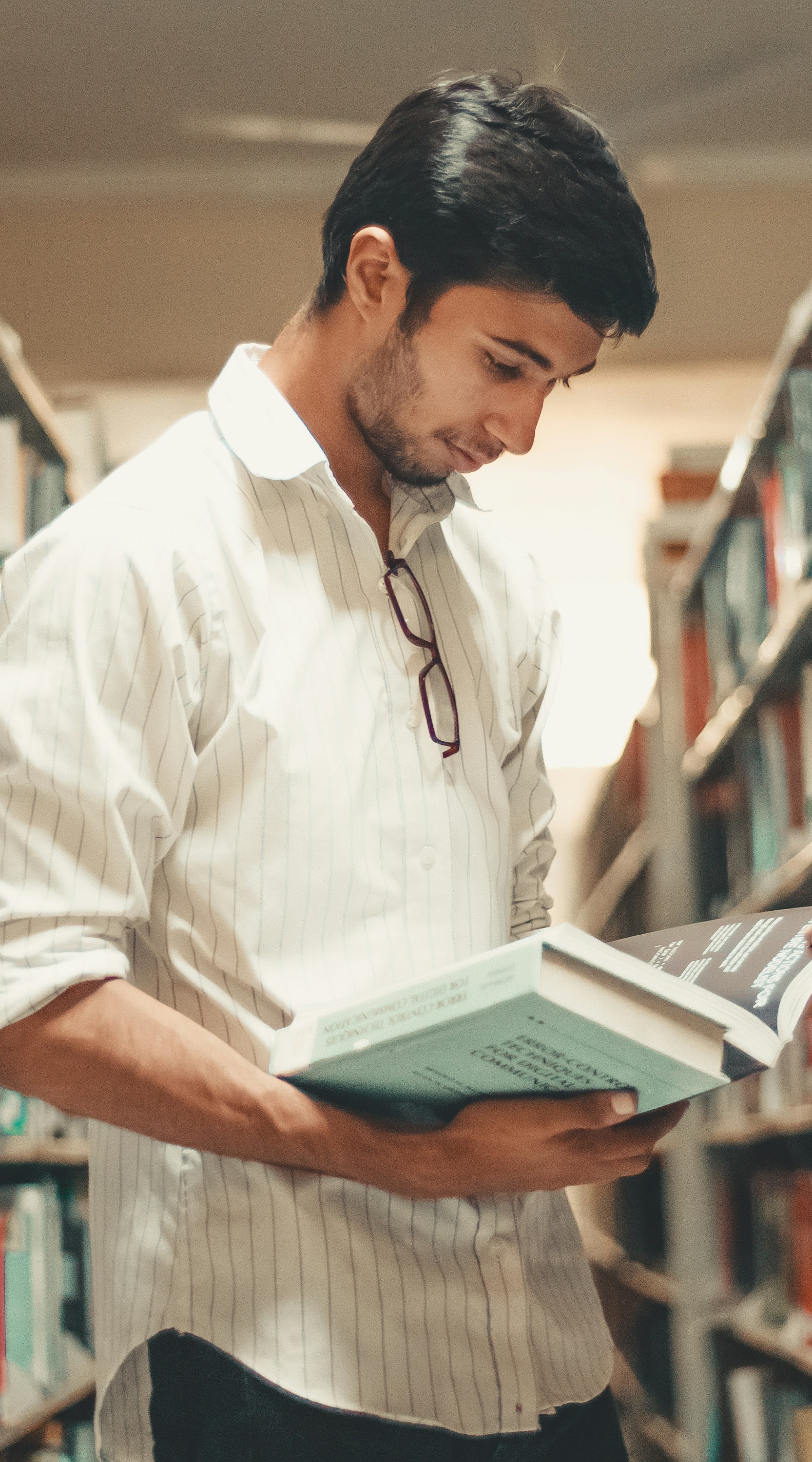 Fotografía de un joven consultando un libro en la biblioteca.